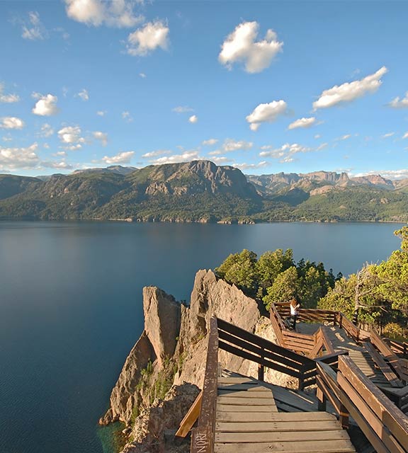A visitor on a pathway overlooking a scenic lake surrounded by mountains near Bariloche.