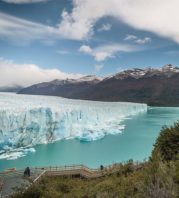 Visitors on a walkway admiring the enormous, blue-colored Perito Moreno glacier.