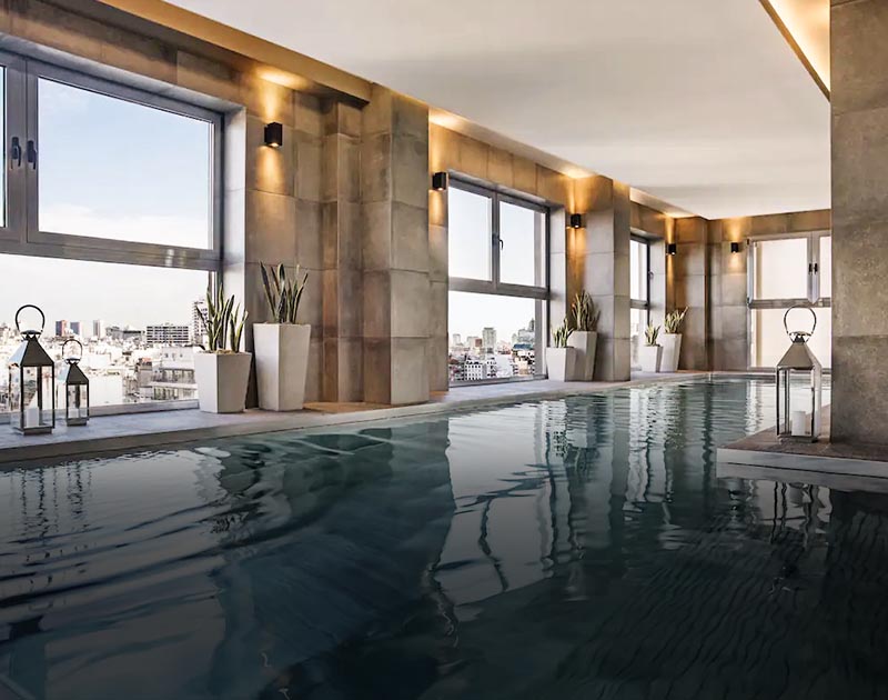 An indoor pool with windows facing out towards the Buenos Aires skyline a the Alvear Palace Hotel.